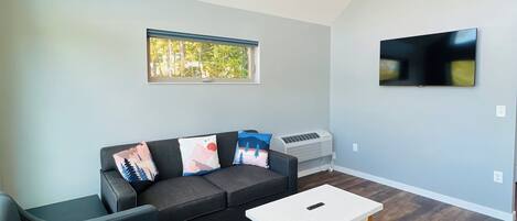 A modern living room with a grey sofa, a white coffee table, and a flat-screen TV mounted on the wall.