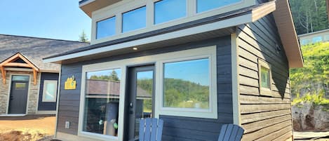 A modern two-story house with a large sliding glass door, a patio with two Adirondack chairs, and a visible address sign.