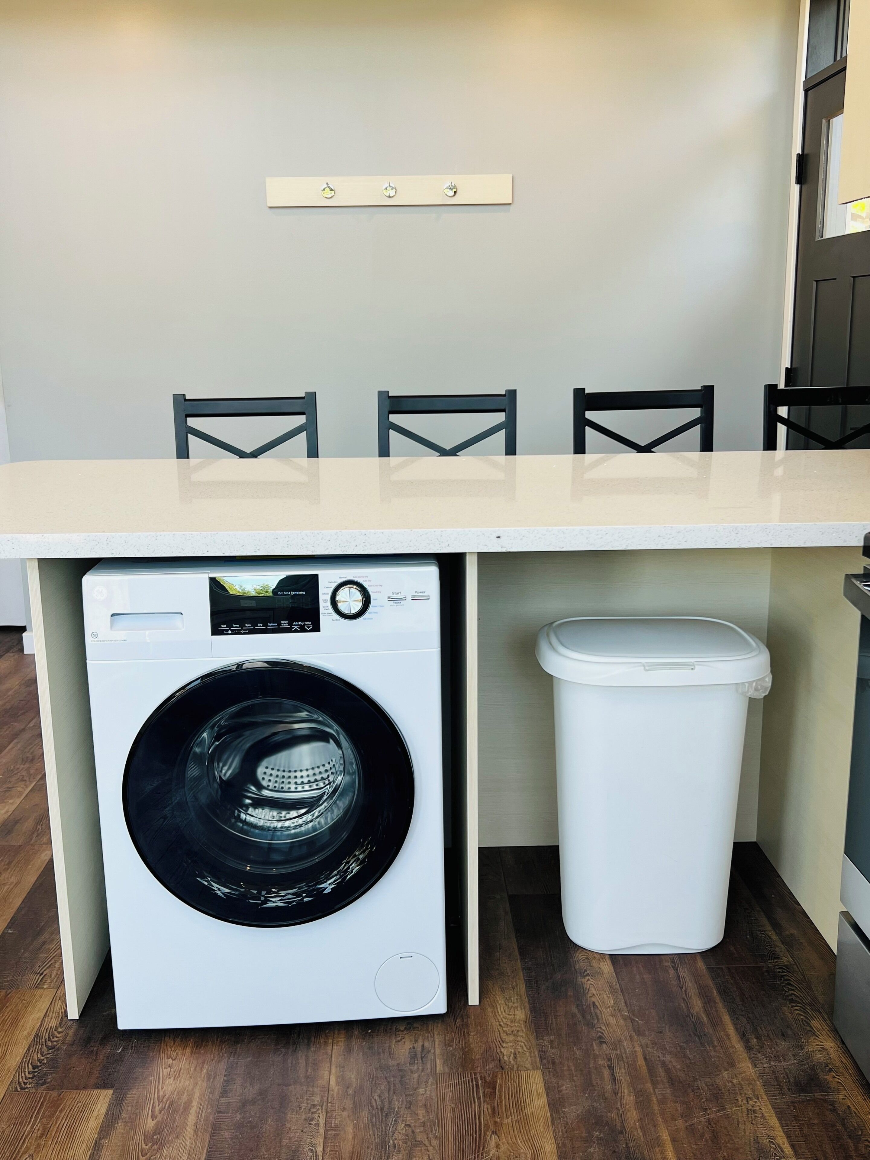 A compact laundry area with a washing machine, a trash bin, and a table with chairs.