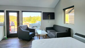 Habitación de hotel moderna con una cama grande, un sofá, una mesita y un televisor. Amplias ventanas con vistas al exterior.