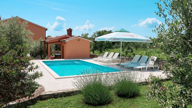A swimming pool with lounge chairs, a covered seating area, and a building with a red roof.