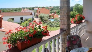 A balcony with a view of a swimming pool, potted plants, and a table with fruit.
