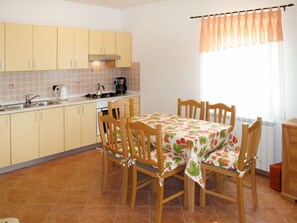 A kitchen with yellow cabinets, a tiled backsplash, a dining table with chairs, and a window with curtains. - Martina by Interhome (Pula/Rakalj)