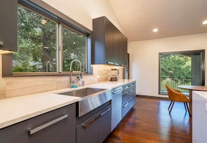 A modern kitchen with a large window, a sink, cabinets, and a dining area with a chair. - Lake Hamilton Dock + Hot Tub + Arcade | Sleeps 16 (Hot Springs)