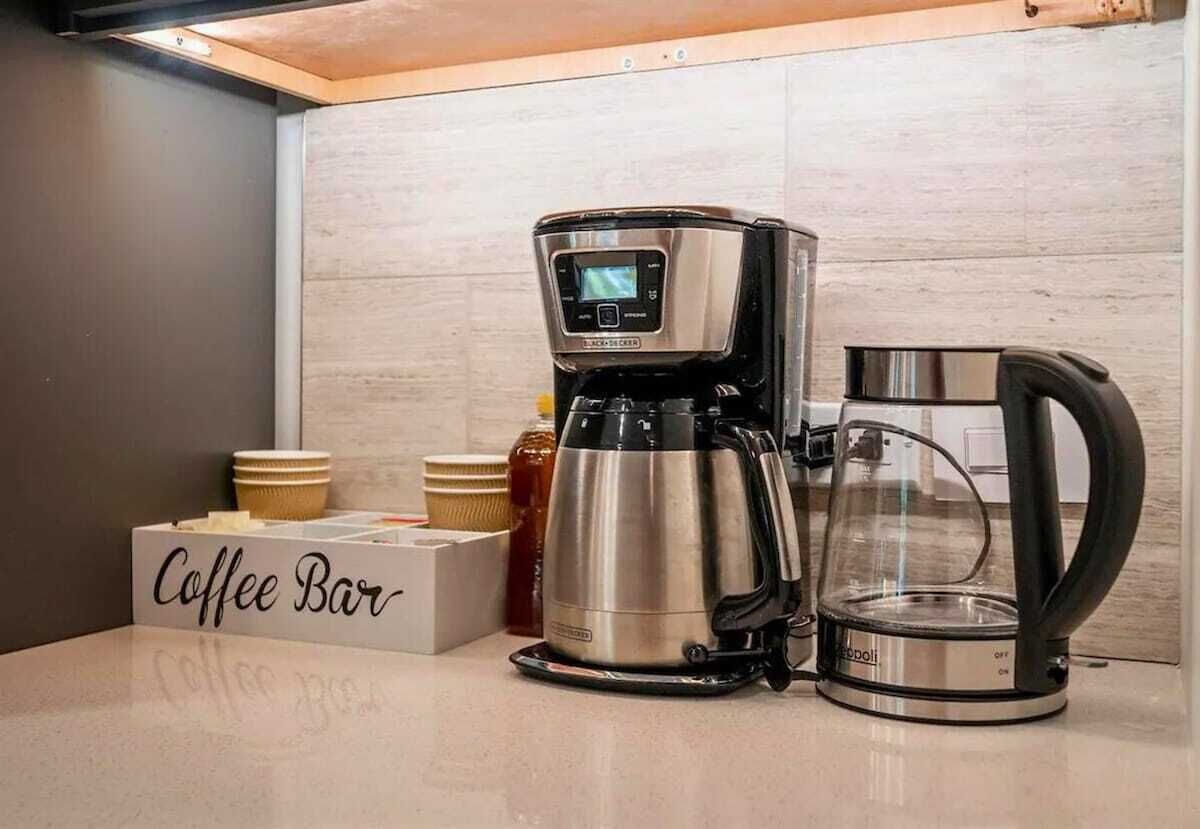 A coffee maker, a glass carafe, and a coffee bar sign on a countertop.