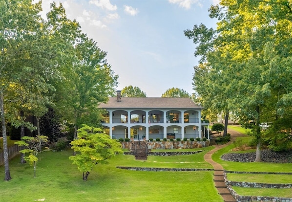 A large, two-story house with a covered porch, surrounded by a well-maintained lawn and trees. - Lake Hamilton Dock + Hot Tub + Arcade | Sleeps 16 (Hot Springs)