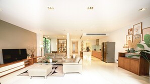 A modern living room with a flat-screen TV, leather sofas, a coffee table, and a dining area with a kitchen in the background.