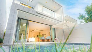 A modern two-story house with a glass door entrance, a visible kitchen area, and a swimming pool in the foreground.