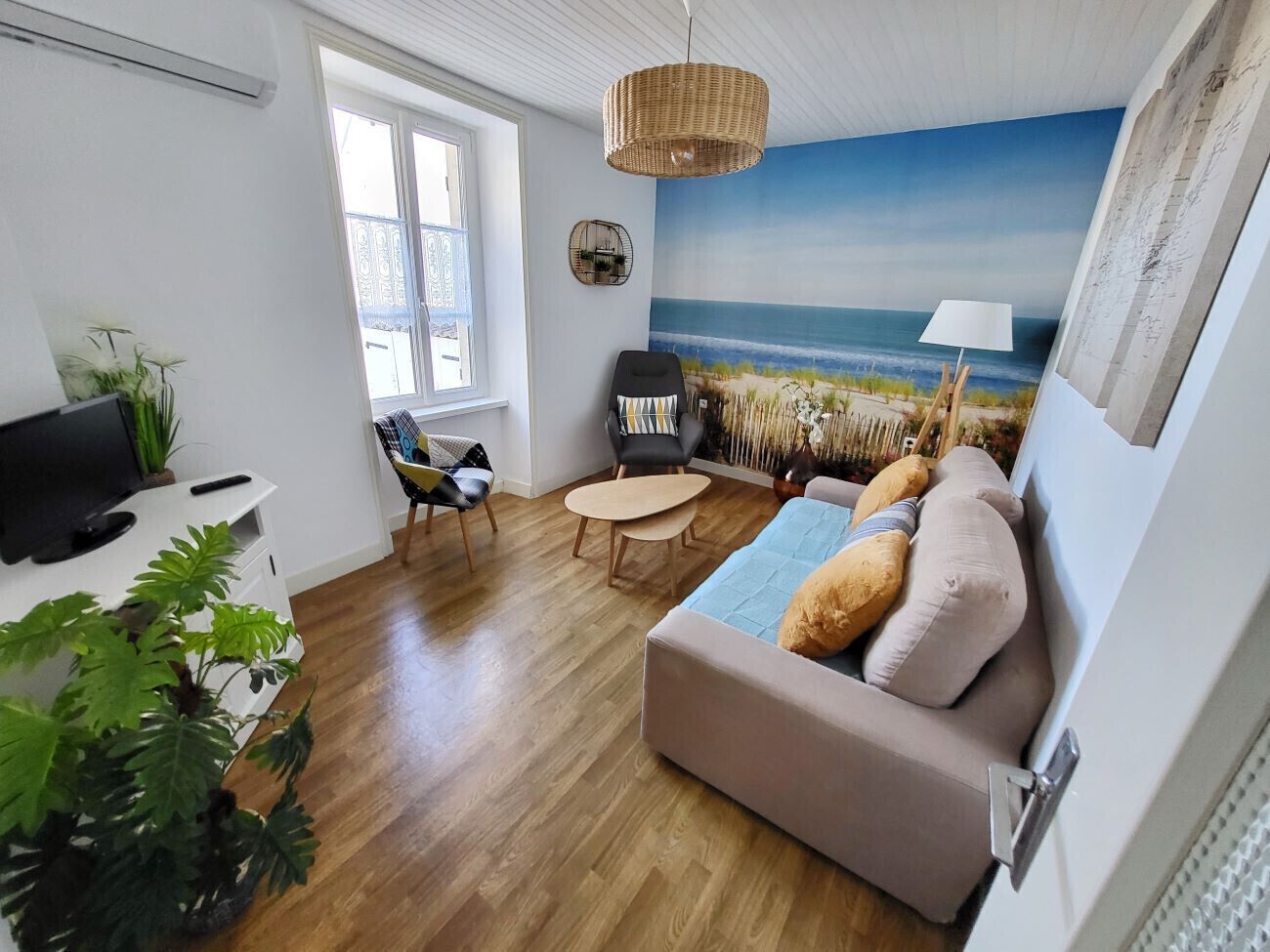 A living room with a beach mural, a sofa, a chair, a small table, and a TV on a white cabinet.