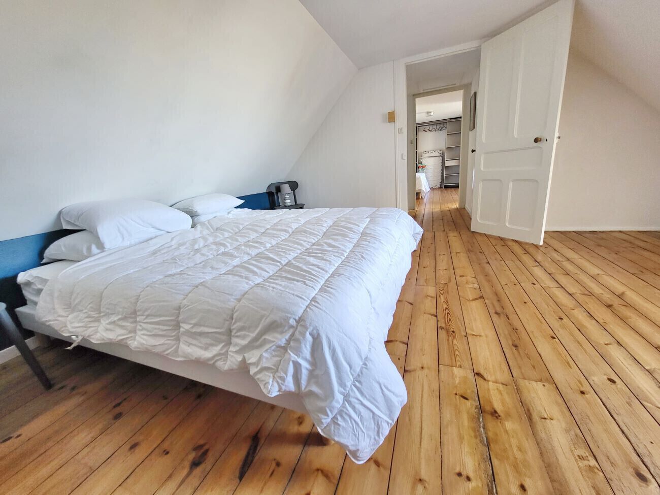 A bedroom with a bed, wooden flooring, and a white door.