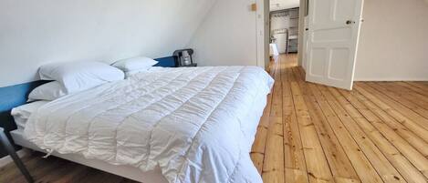 A bedroom with a bed, wooden flooring, and a white door.