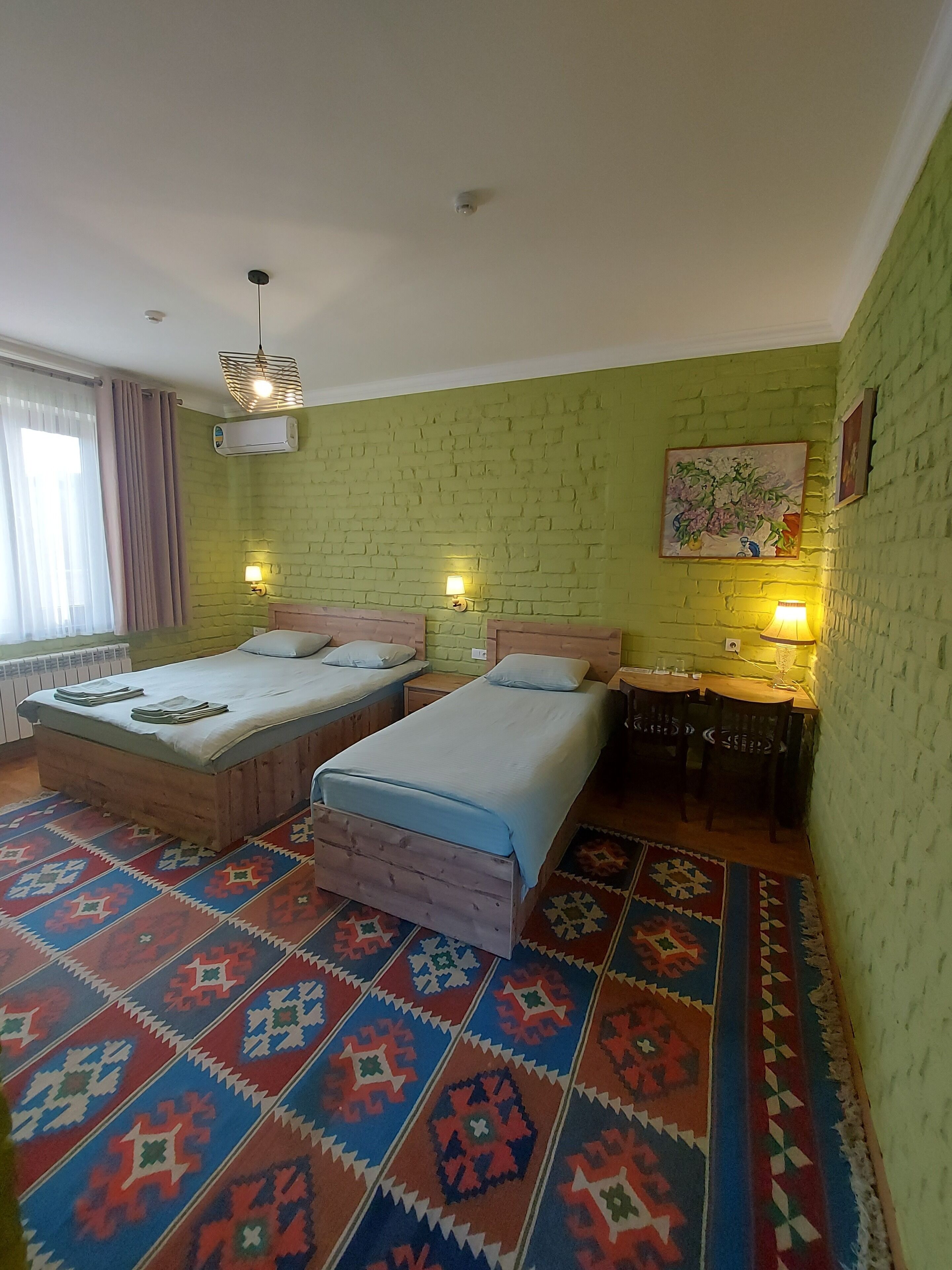 Una habitación con dos camas, un tapete estampado, una pared de ladrillo y un cuadro.