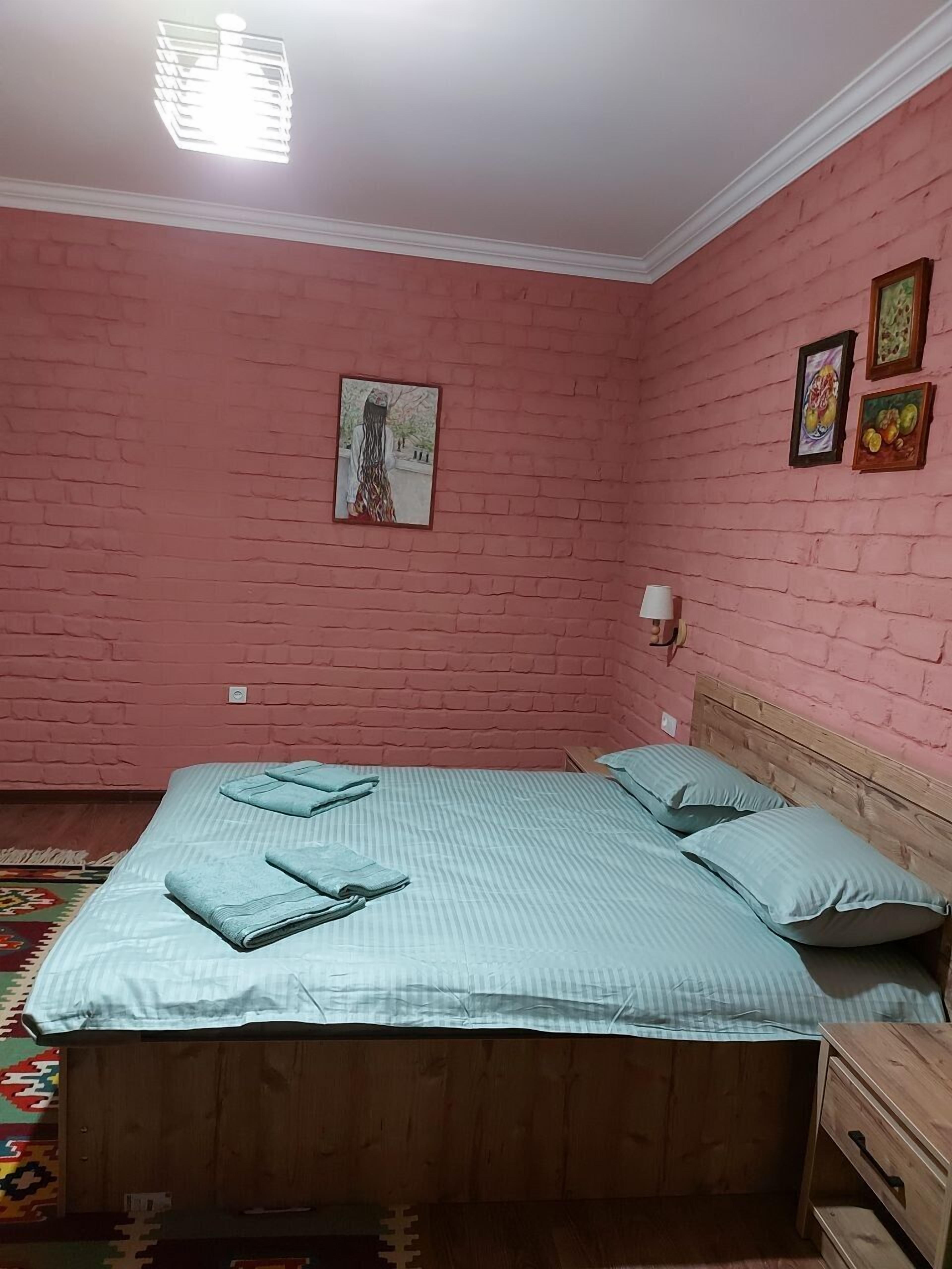 Un dormitorio con cama de madera, paredes de ladrillo rosa y una lámpara en el techo.
