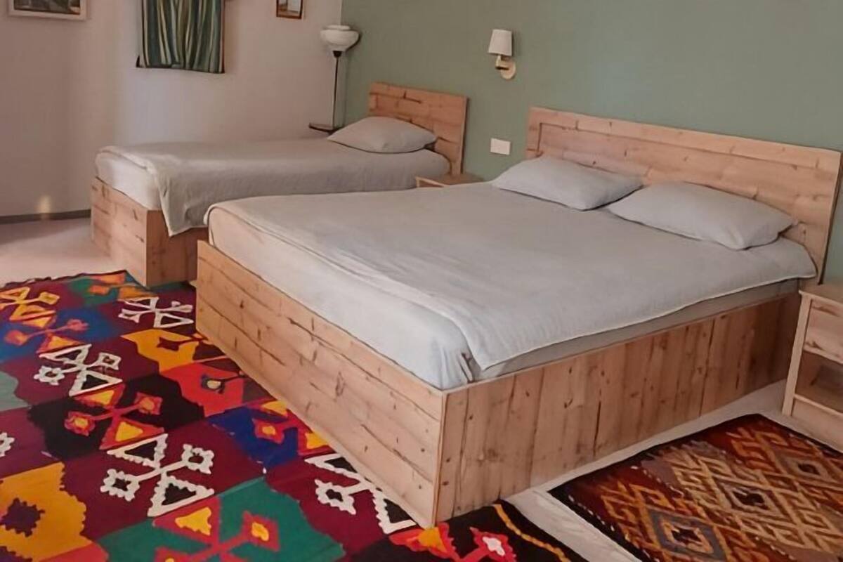 Une chambre avec deux lits en bois, un tapis coloré et une table de chevet avec une lampe.