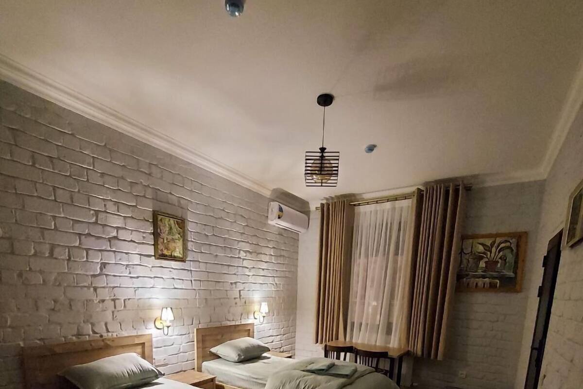 Une chambre avec deux lits, un mur en briques, un tapis à motifs et un ventilateur de plafond.