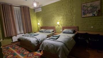 A room with two beds, a patterned rug, a green brick wall, and a painting.