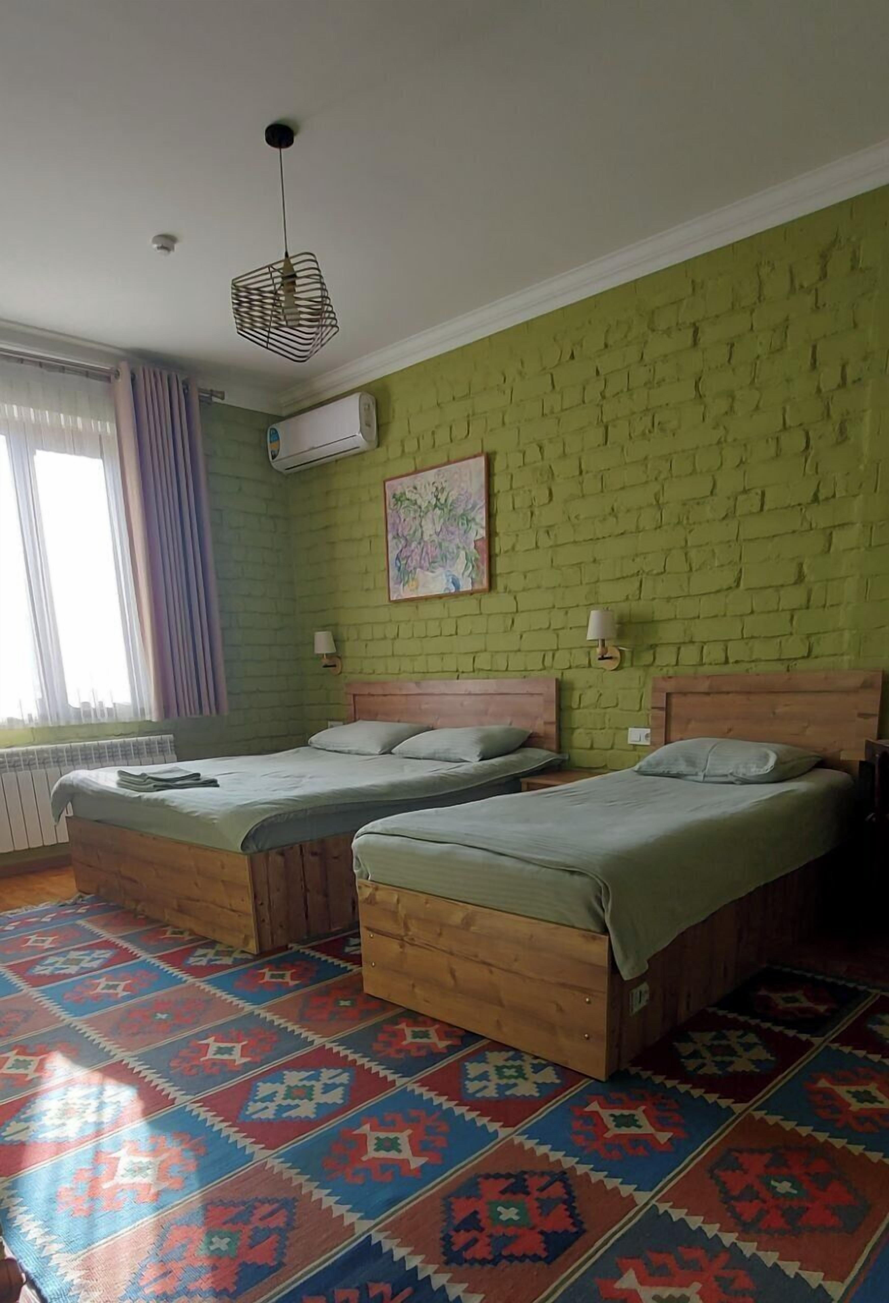 A room with two wooden beds, a patterned carpet, and a green brick wall.