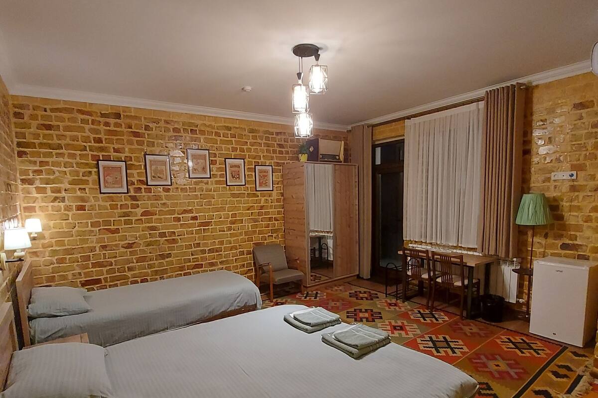 Une chambre avec deux lits, un mur en briques, un tapis à motifs, un bureau et une chaise.