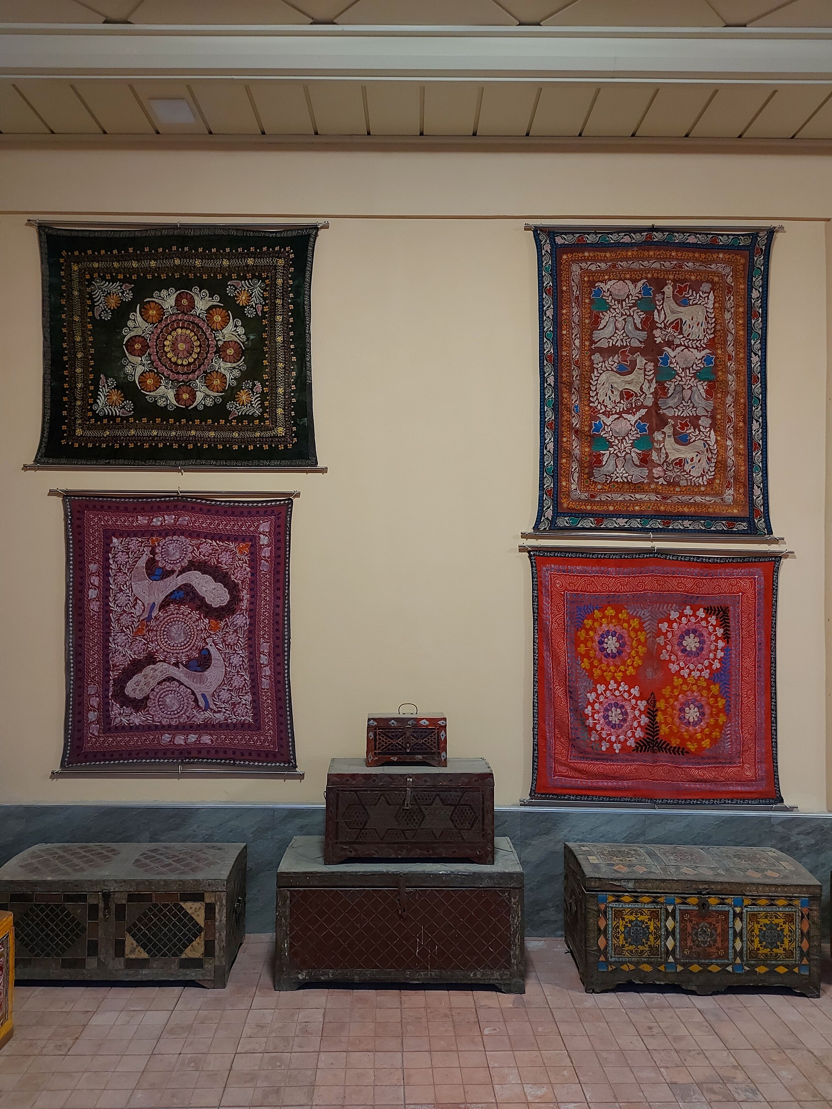 Uma parede com quatro grandes tapeçarias coloridas e três pequenos baús decorados.
