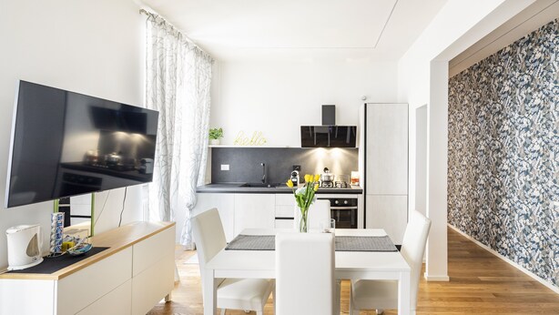 Eine moderne Küche mit Flachbildfernseher, weißen Schränken und einem Essbereich mit weißem Tisch und Stühlen.
