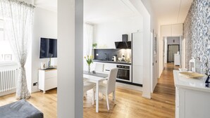 Eine moderne Küche mit weißen Schränken, einem schwarzen Herd und einem Essbereich mit weißem Tisch und Stühlen.