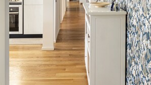 Eine moderne Küche mit weißen Schränken, Holzboden und einer Wand mit Muster-Tapete auf der rechten Seite.