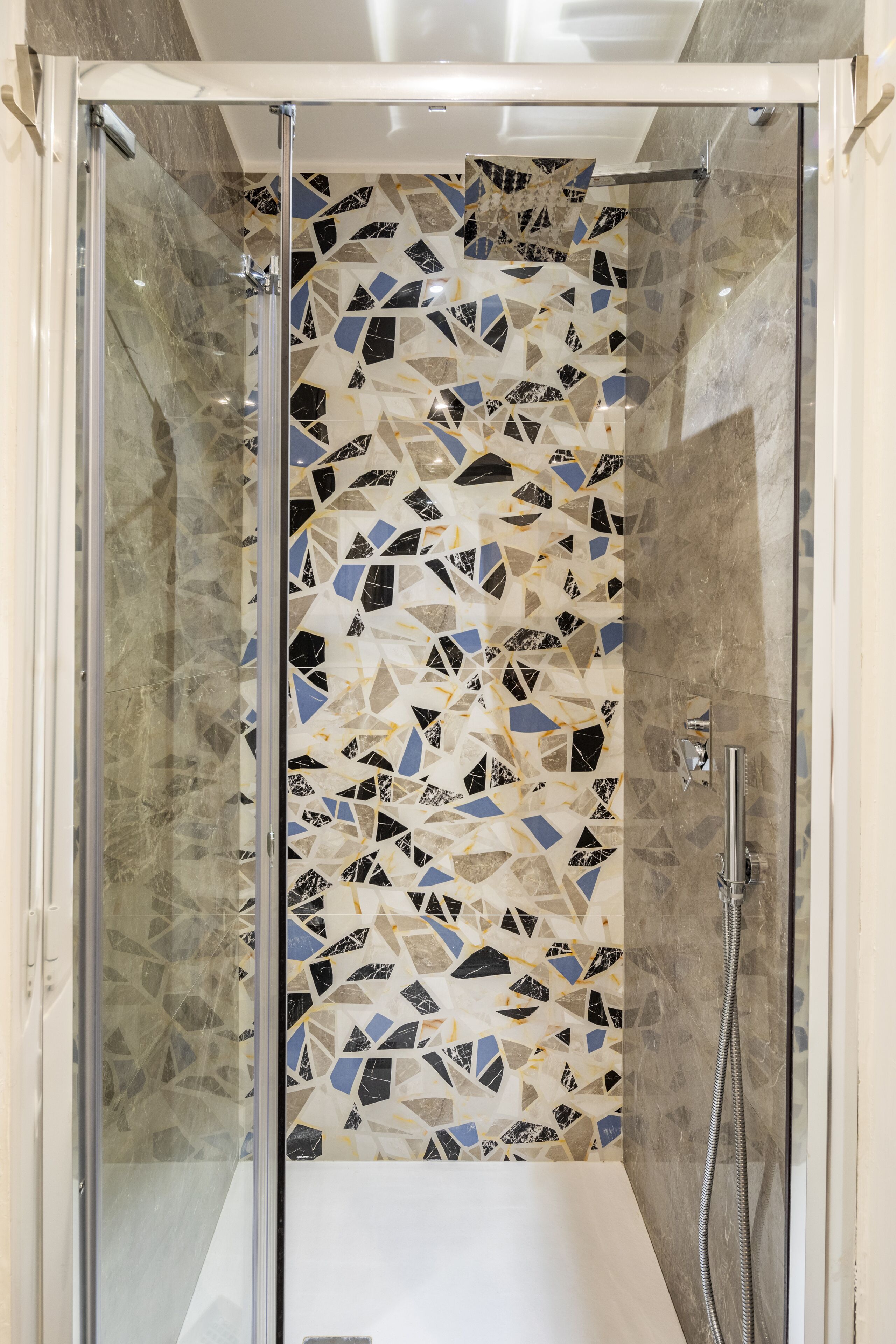 Une douche avec un mur recouvert de mosaïques et un pommeau de douche à main.