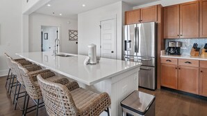 Una cocina moderna con una isla grande, electrodomésticos de acero inoxidable, armarios de madera y un salpicadero de baldosas en patrón de espiga.