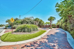 A paved walkway with a pedestrian crossing sign, surrounded by lush greenery and palm trees. - Spacious 30A Retreat Near Private Beach Access & Heated Pool (Santa Rosa Beach)