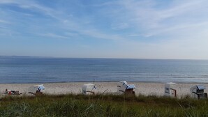Une plage avec plusieurs chaises de plage et des parasols, une personne prenant une photo et une vue dégagée sur l’océan.