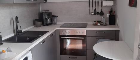 A compact kitchen with a washing machine, a sink, a stove, and a small dining area with a table and chairs.