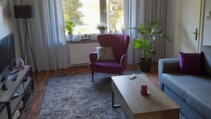 Un salon comprenant un canapé, un fauteuil, une table basse et une grande fenêtre avec des rideaux.