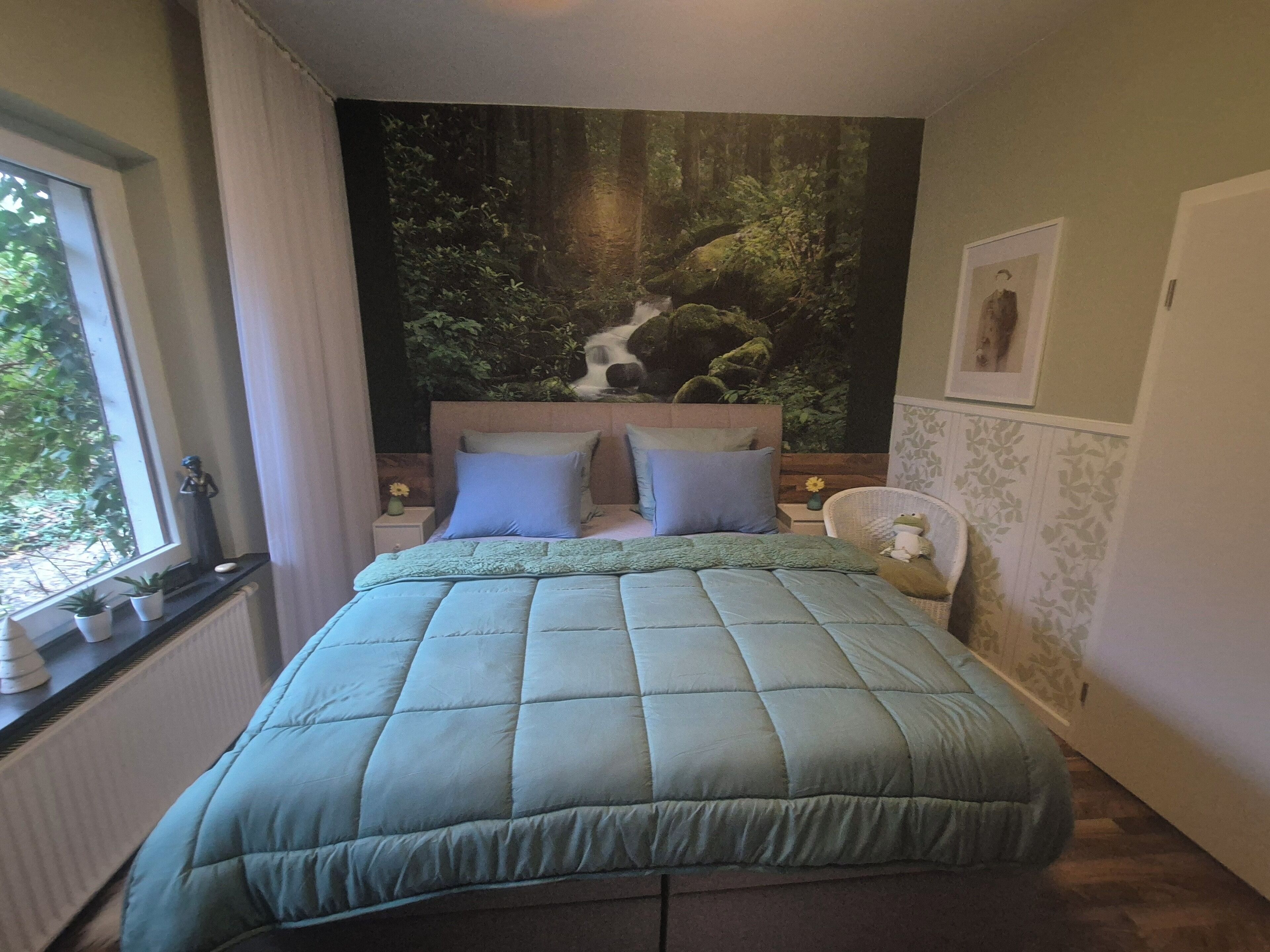 Une chambre à coucher avec un lit, une fenêtre, une fresque murale et une petite table sur laquelle est posé un vase.