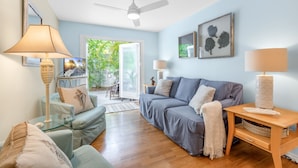 Ein Wohnzimmer mit einer Couch, einem Glastisch, einer Lampe und einem Deckenventilator.