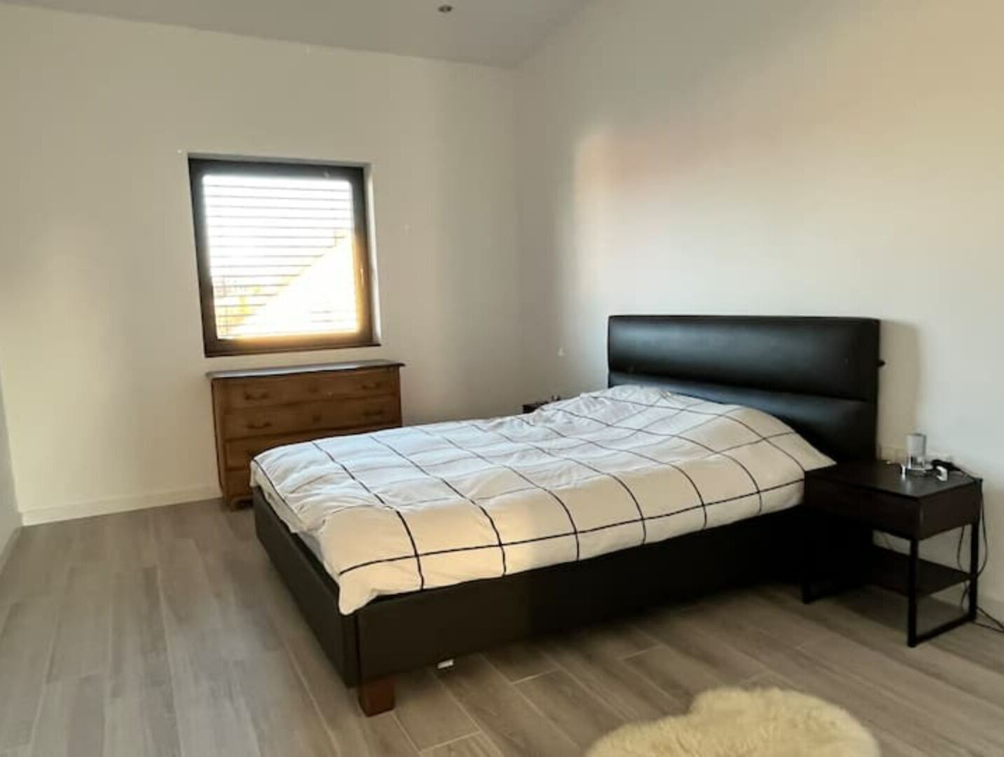 A bedroom with a bed, a dresser, a nightstand, and a window.
