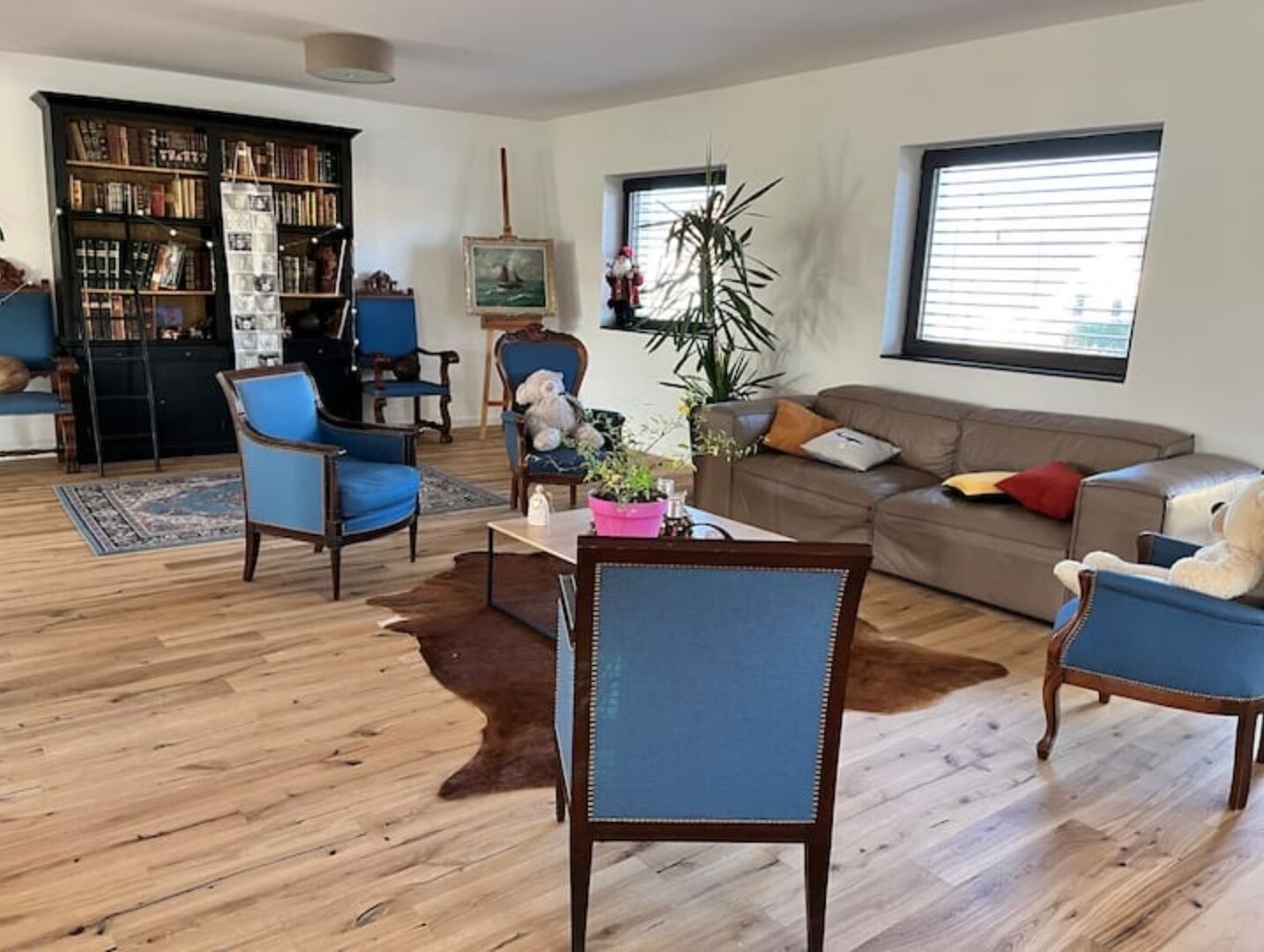A living room with a wooden floor, a sofa, two armchairs, a coffee table, a bookshelf, and a painting.