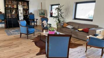 A living room with a wooden floor, a sofa, two armchairs, a coffee table, a bookshelf, and a painting.