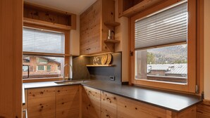 A wooden kitchen with built-in cabinets, a stainless steel sink, and a window with a view of a cabin. - Casa Ca Dei Pini, surrounded by Nature (Cortina d´Ampezzo)