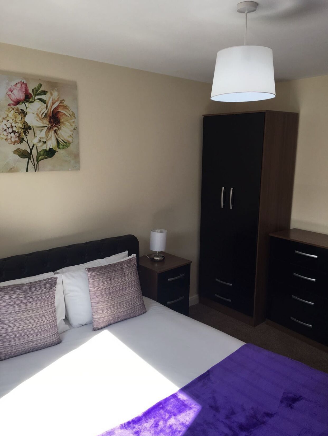 Ein Schlafzimmer mit einem Bett, einem Nachttisch, einem Kleiderschrank und einer Pendelleuchte.