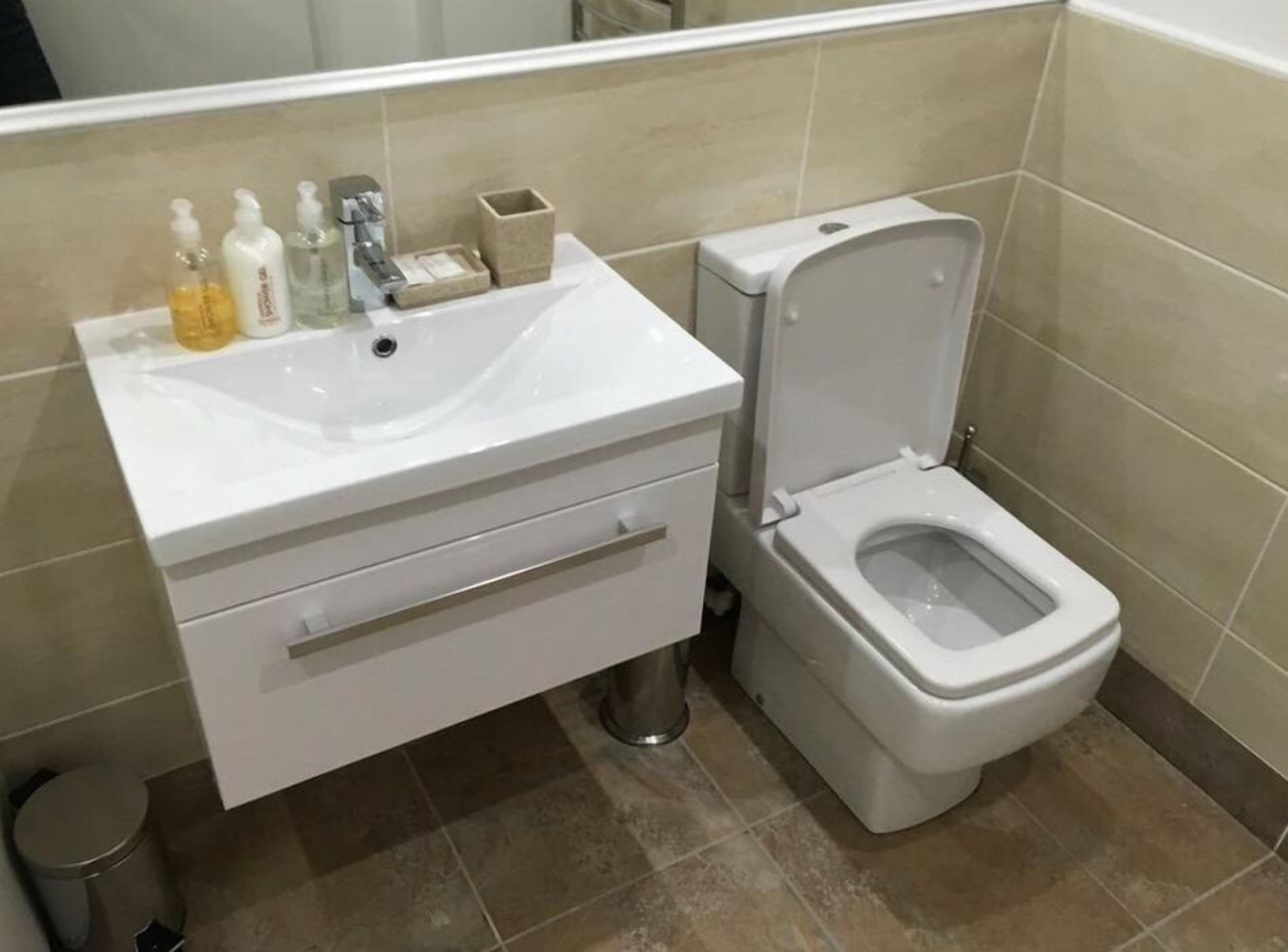 Un baño con lavamanos, inodoro y un cubo de basura blancos.