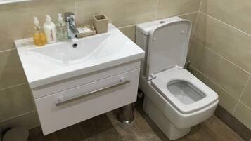 Un baño con lavamanos, inodoro y un cubo de basura blancos.