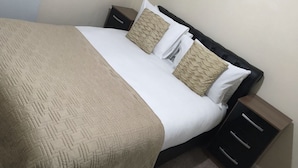 A neatly made bed with a patterned bedspread and two pillows, flanked by dark wooden nightstands with drawers. - Ch & bro properties Ltd (Leeds)