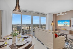 Una camera d'albergo moderna con balcone, angolo ristoro, divano, TV e vista sulla città.