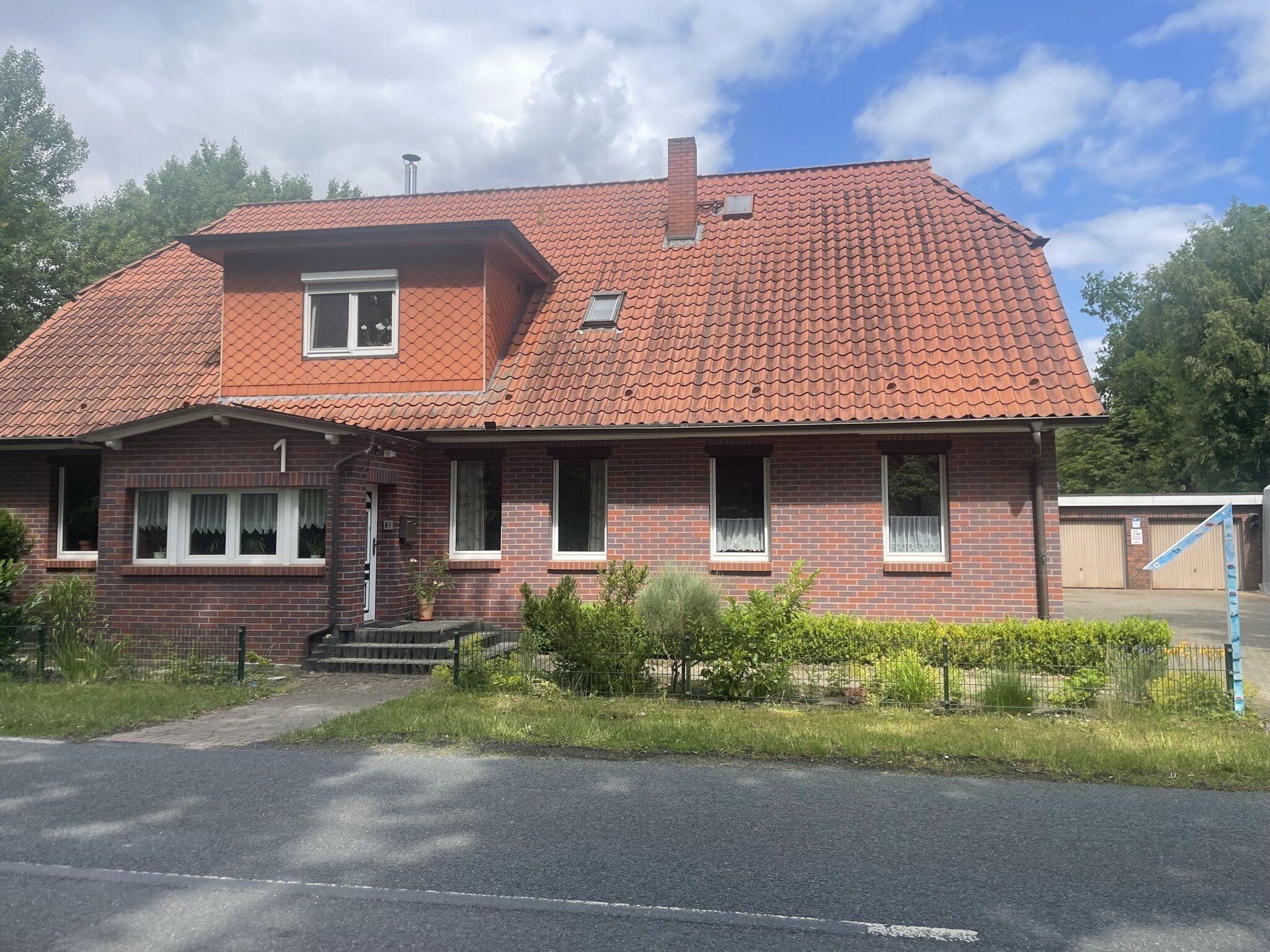 A two-story brick house with a red-tiled roof, a front porch, and a small front yard.