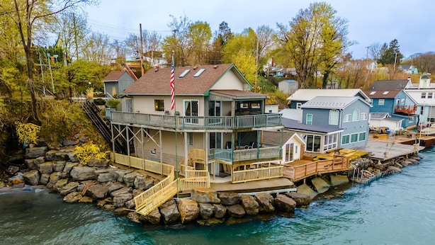 Une maison située au bord de l’eau, dotée d’un balcon, d’un drapeau et d’une jetée qui s’avance dans l’eau.