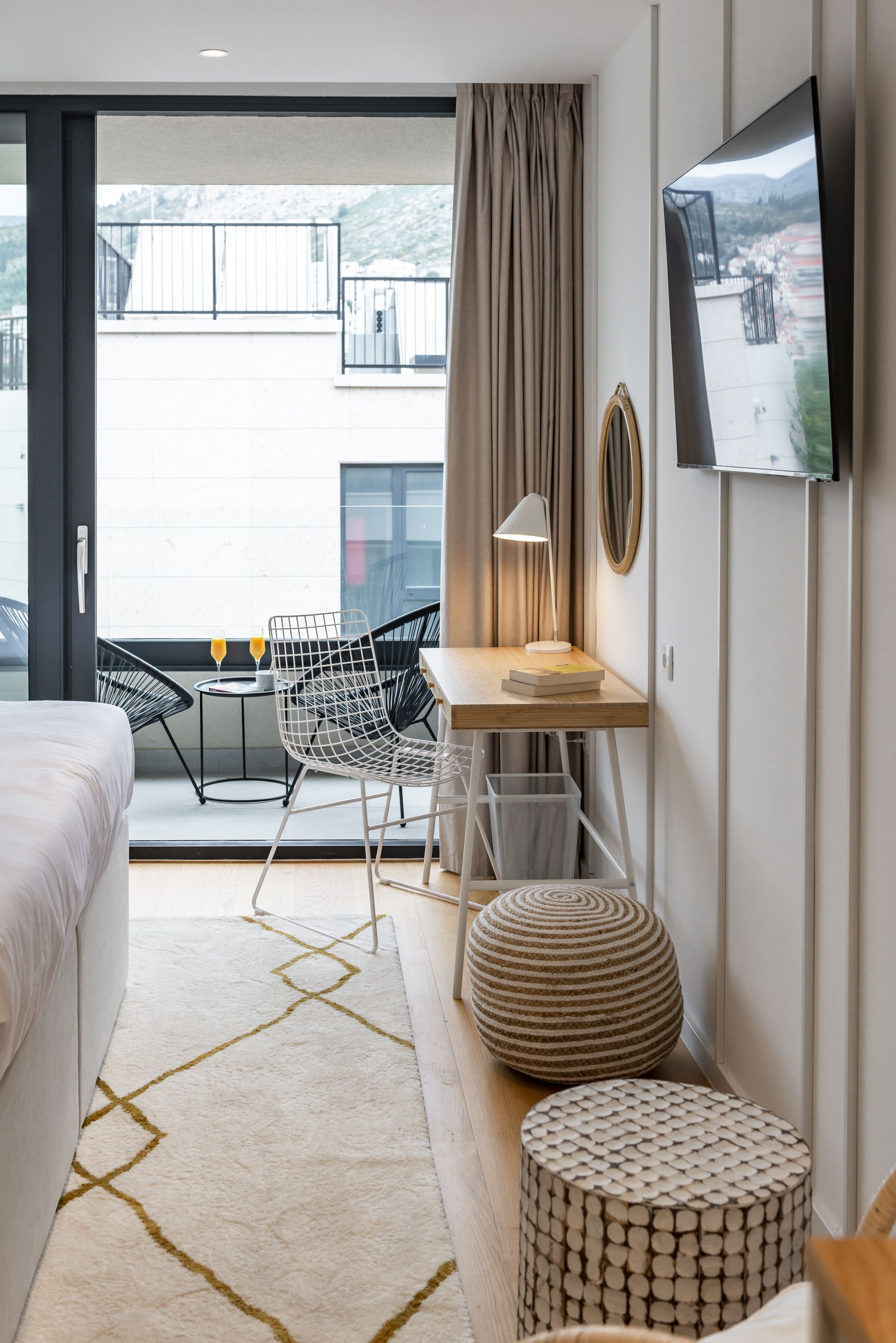 Ein modernes Hotelzimmer mit Bett, Schreibtisch, Stuhl, Fernseher und einem Balkon mit Blick.