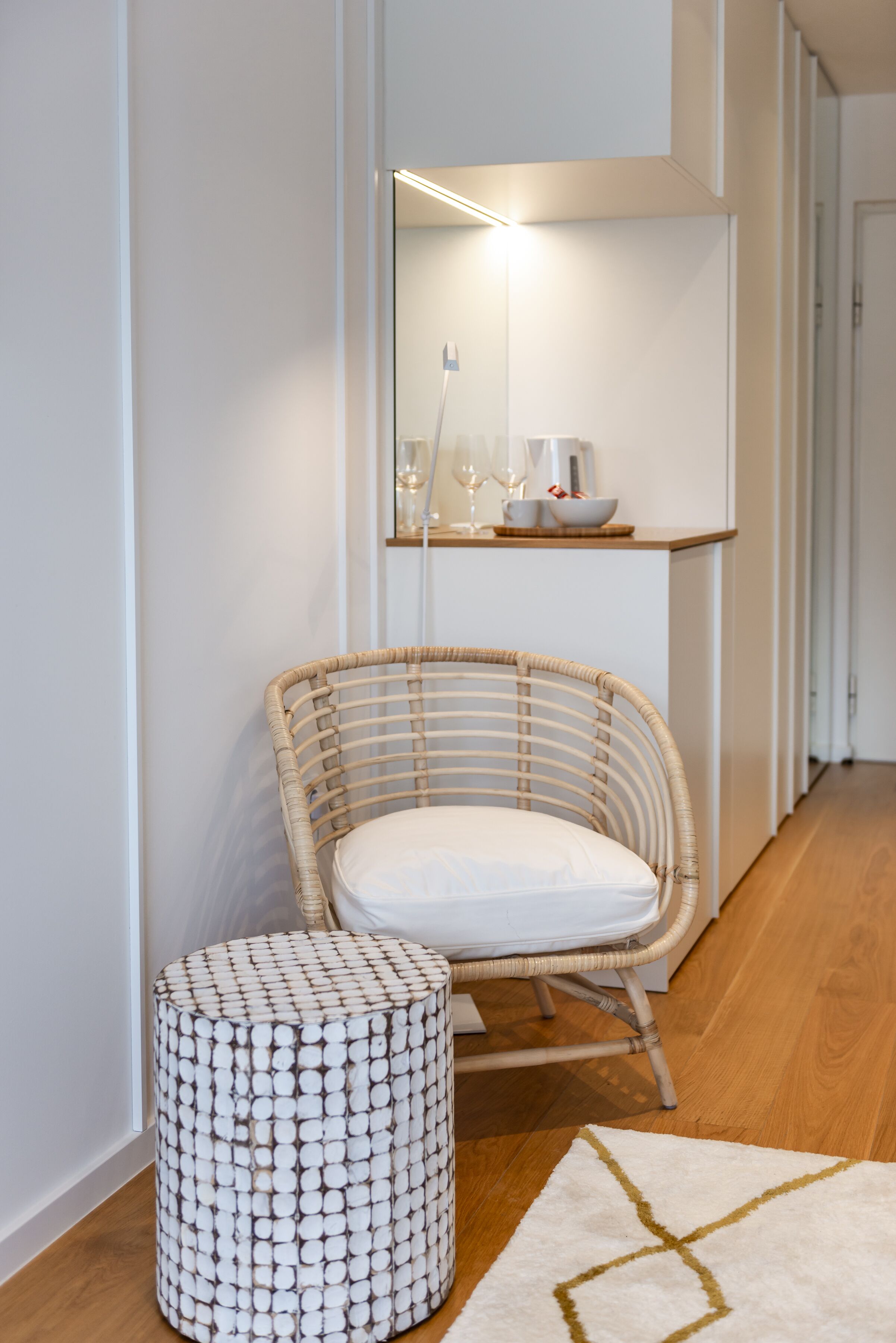 A wicker chair with a white cushion, a round ottoman, and a white rug with a geometric pattern.