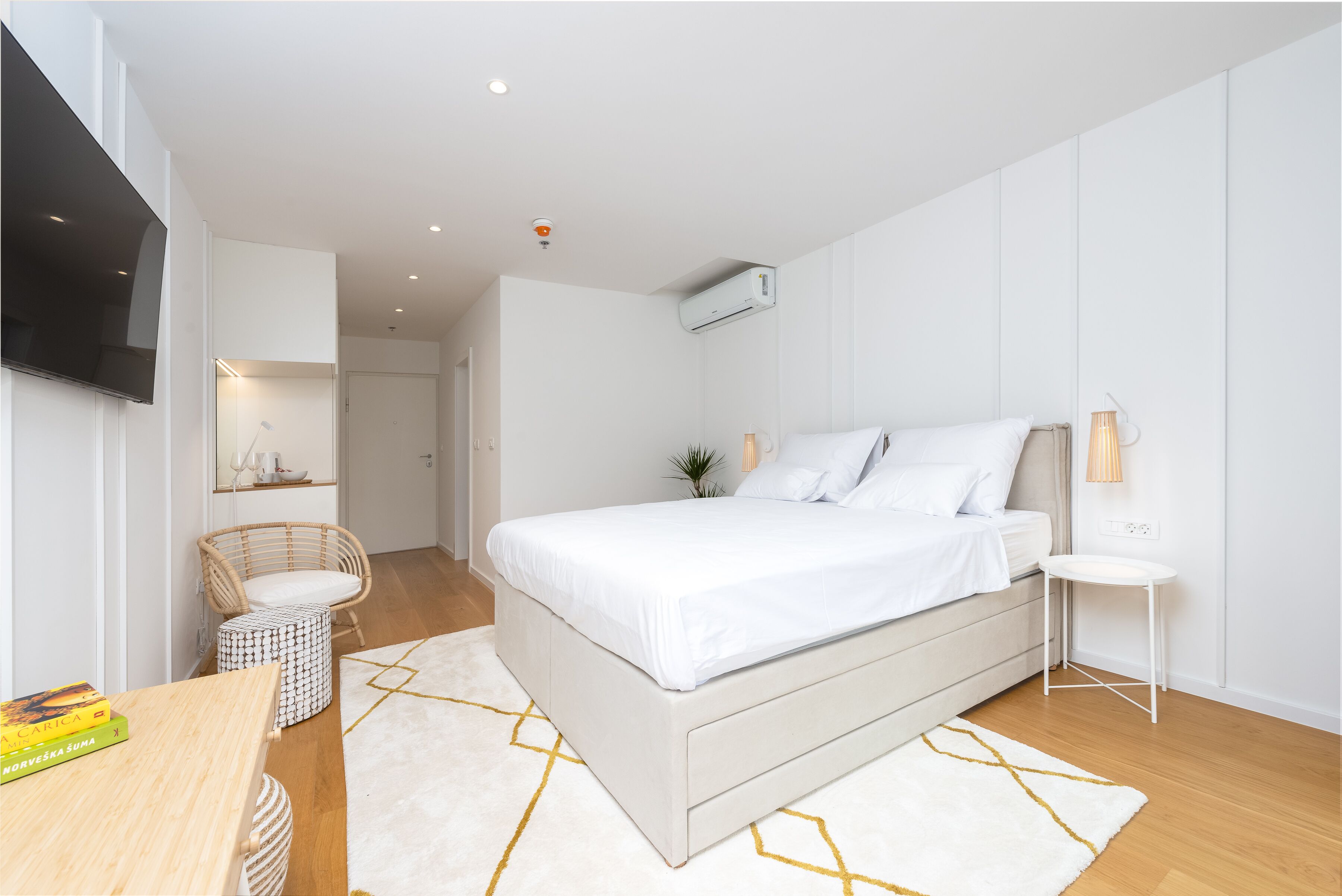 A modern bedroom with a large bed, a flat-screen TV mounted on the wall, a small side table, and a chair.