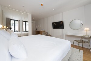 Una habitación de hotel moderna con una cama grande, un escritorio, una silla, un televisor y un espejo.