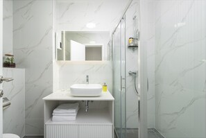 A modern bathroom with a white marble sink, a glass shower enclosure, and a white vanity. - City Residences (Dubrovnik)
